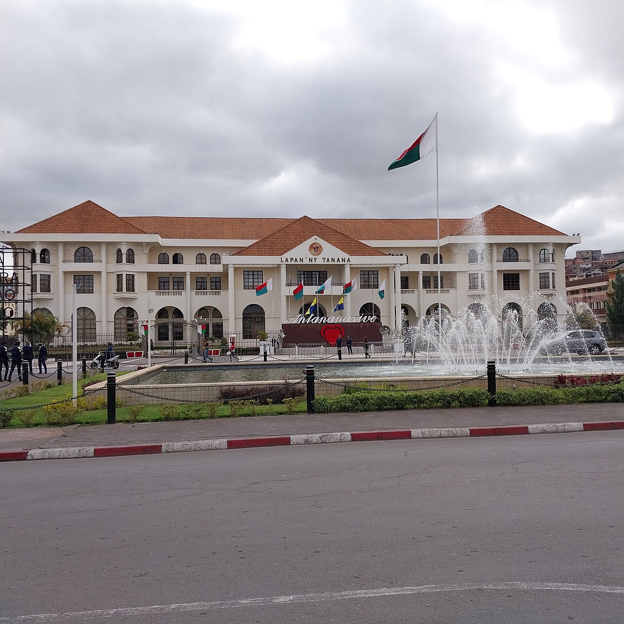 Antananarivo City Hall, a white building with red-tiled roofs, a fountain and a Malagasy flag, seen from the street