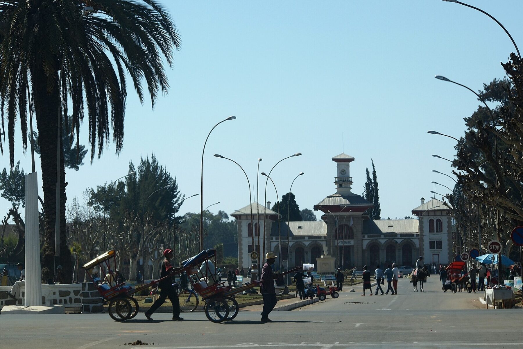 The historic railway station building in Antsirabe, Madagascar, with pulled rickshaws crossing the avenue in front