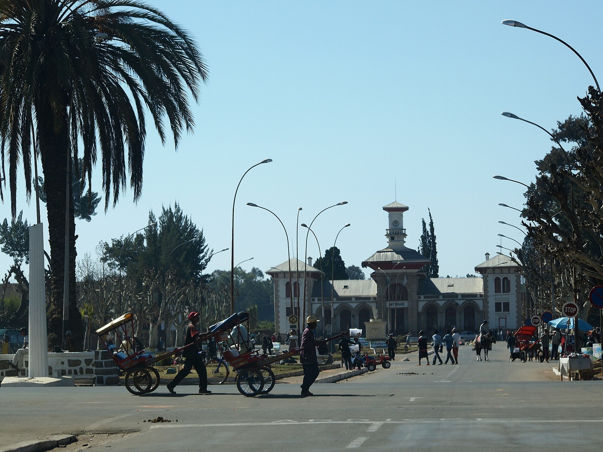 The historic railway station building in Antsirabe, Madagascar, with pulled rickshaws crossing the avenue in front