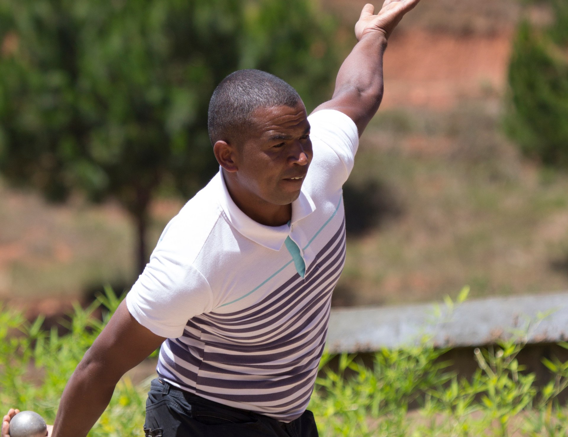 A Madagascar pétanque player stretches an arm back as he prepares to throw a boule