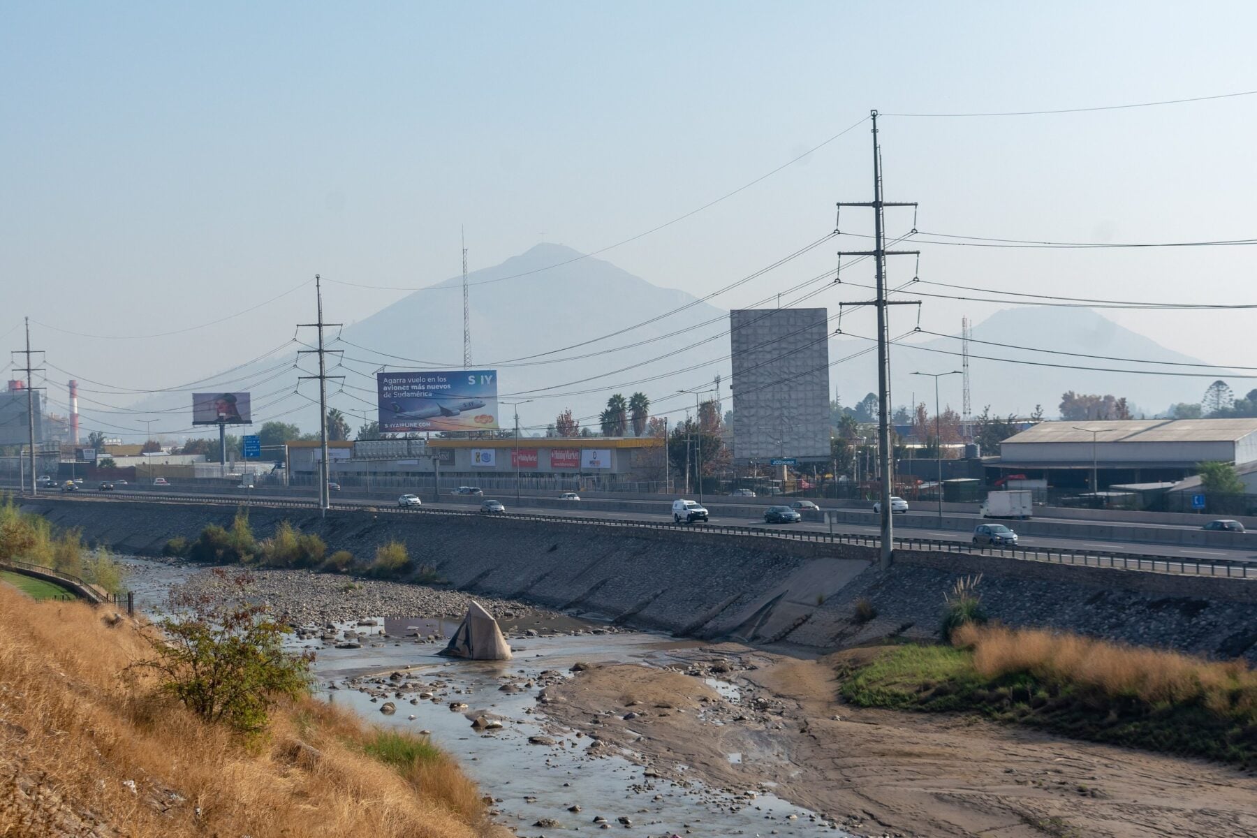 A motorway and river channel in Renca, a district of Santiago, Chile, with hills behind