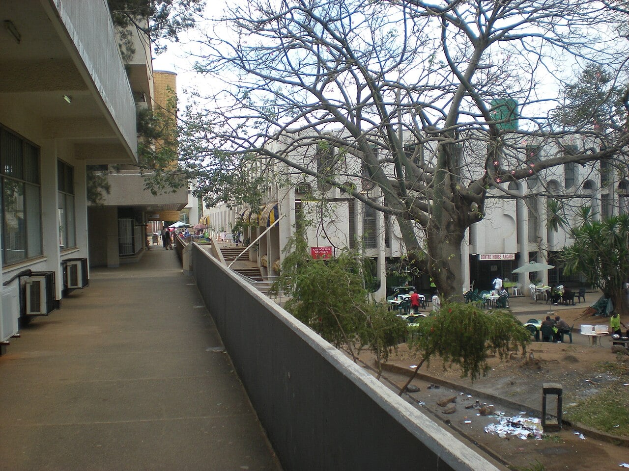 Centre House Arcade shopping and office complex in central Lilongwe, Malawi, with a bare tree and people at outdoor tables