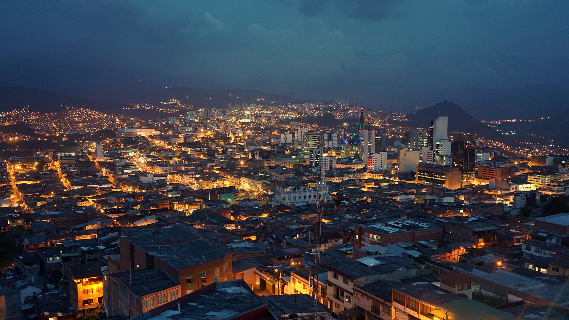 Manizales city centre lit up at dusk, seen from the Chipre lookout, with the illuminated cathedral tower and Andean hills