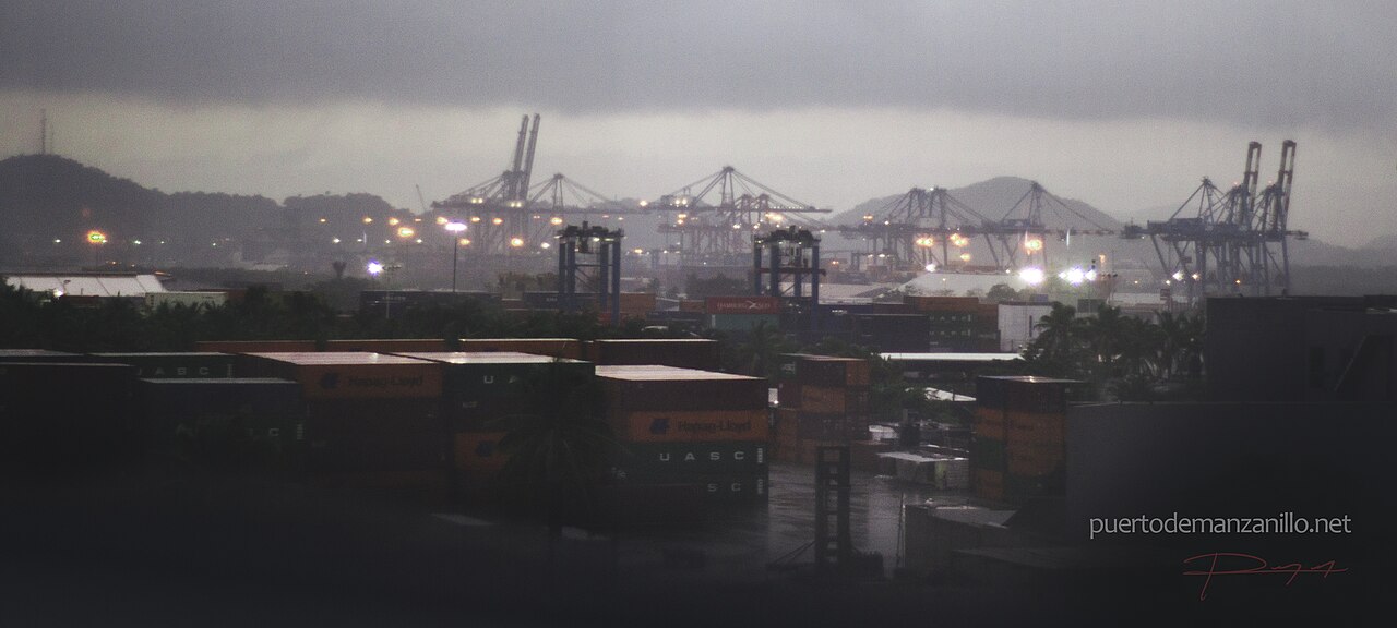 Container cranes and stacked shipping containers at the port of Manzanillo on Mexico's Pacific coast under a grey sky