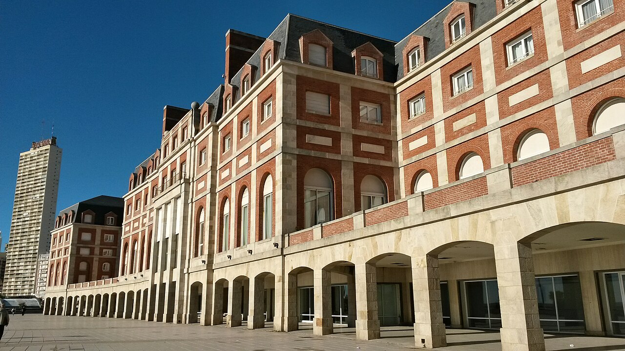 Red-brick and stone facade of the Hotel Provincial with arched arcades on the Mar del Plata seafront under a clear blue sky