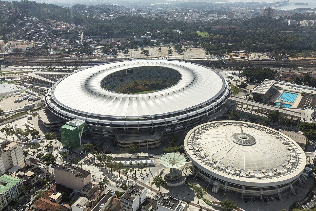 The Maracanã stadium and the Maracanãzinho arena seen from above, with the railway and green hills of Rio behind.