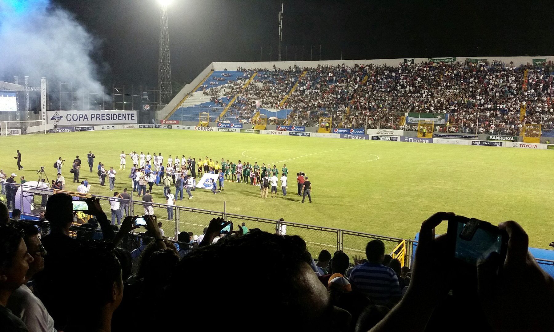 Players and officials line up on the pitch before a match under floodlights at the Estadio Francisco Morazán in San Pedro Sula, Honduras