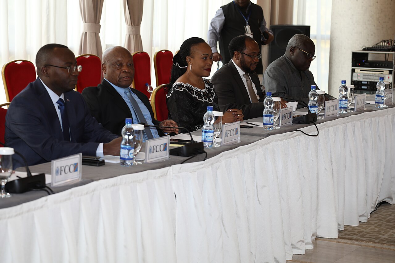 Marie-Ange Mushobekwa sits with four men at a conference table behind FCC name cards and water bottles