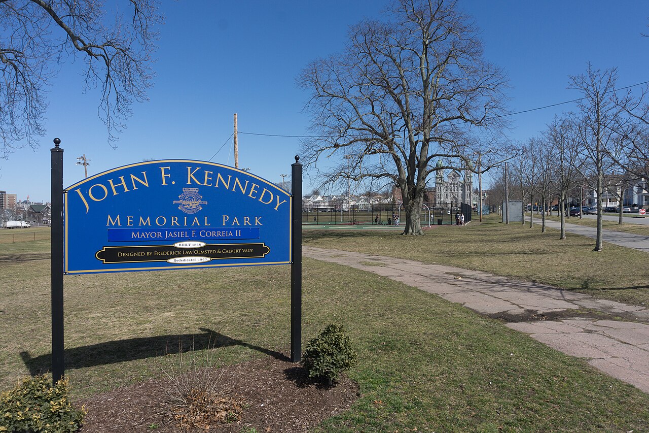 Sign at John F. Kennedy Memorial Park in Fall River, Massachusetts, with a church and houses behind
