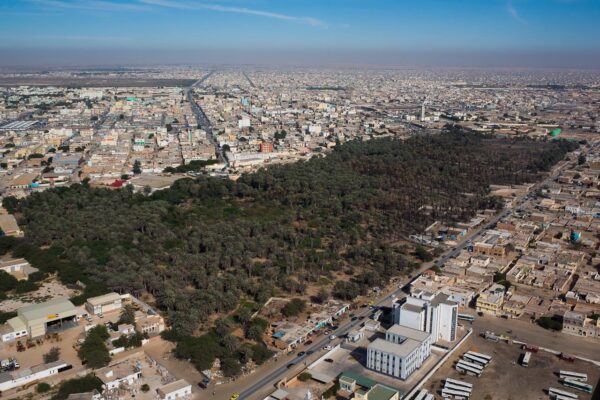 Aerial view of Nouakchott with a date palm grove, low-rise streets and a bus depot under a hazy sky
