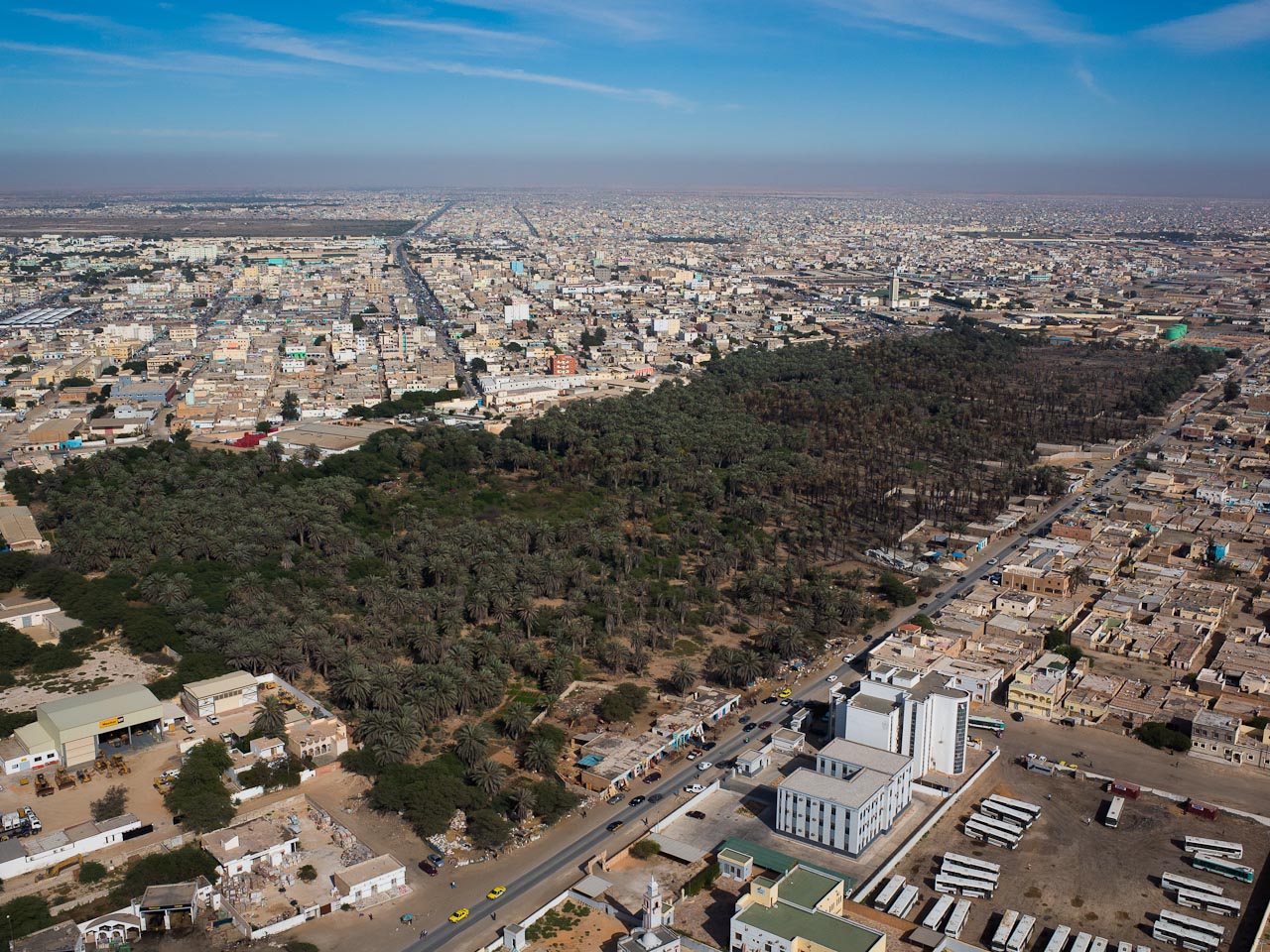 Aerial view of Nouakchott with a date palm grove, low-rise streets and a bus depot under a hazy sky