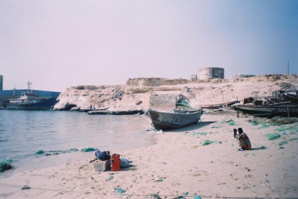 Sandy shore at Nouadhibou, Mauritania, with a moored ship, a sandstone cliff and fishing boats on the beach