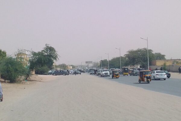 A wide road in Nouakchott, the capital of Mauritania, with cars and yellow auto-rickshaws under a hazy sky