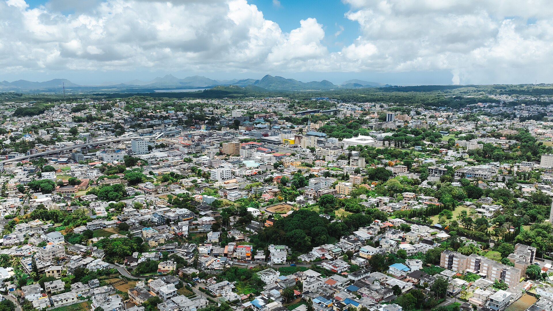 Aerial view of Curepipe, a highland town in central Mauritius, with rooftops, trees and mountains on the horizon