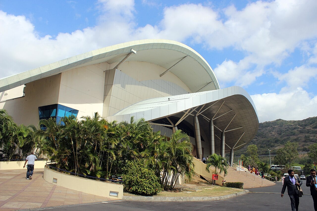 The curved white roof of the Swami Vivekananda International Convention Centre at Pailles, Mauritius, with palm trees and hills behind