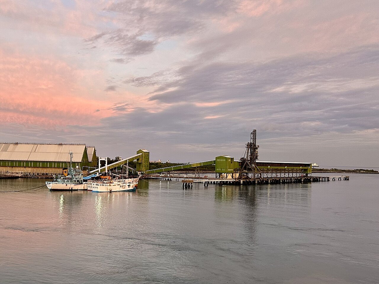 The green conveyor gantries and warehouses of the bulk sugar terminal on the quay in Port Louis harbour under a pink sky