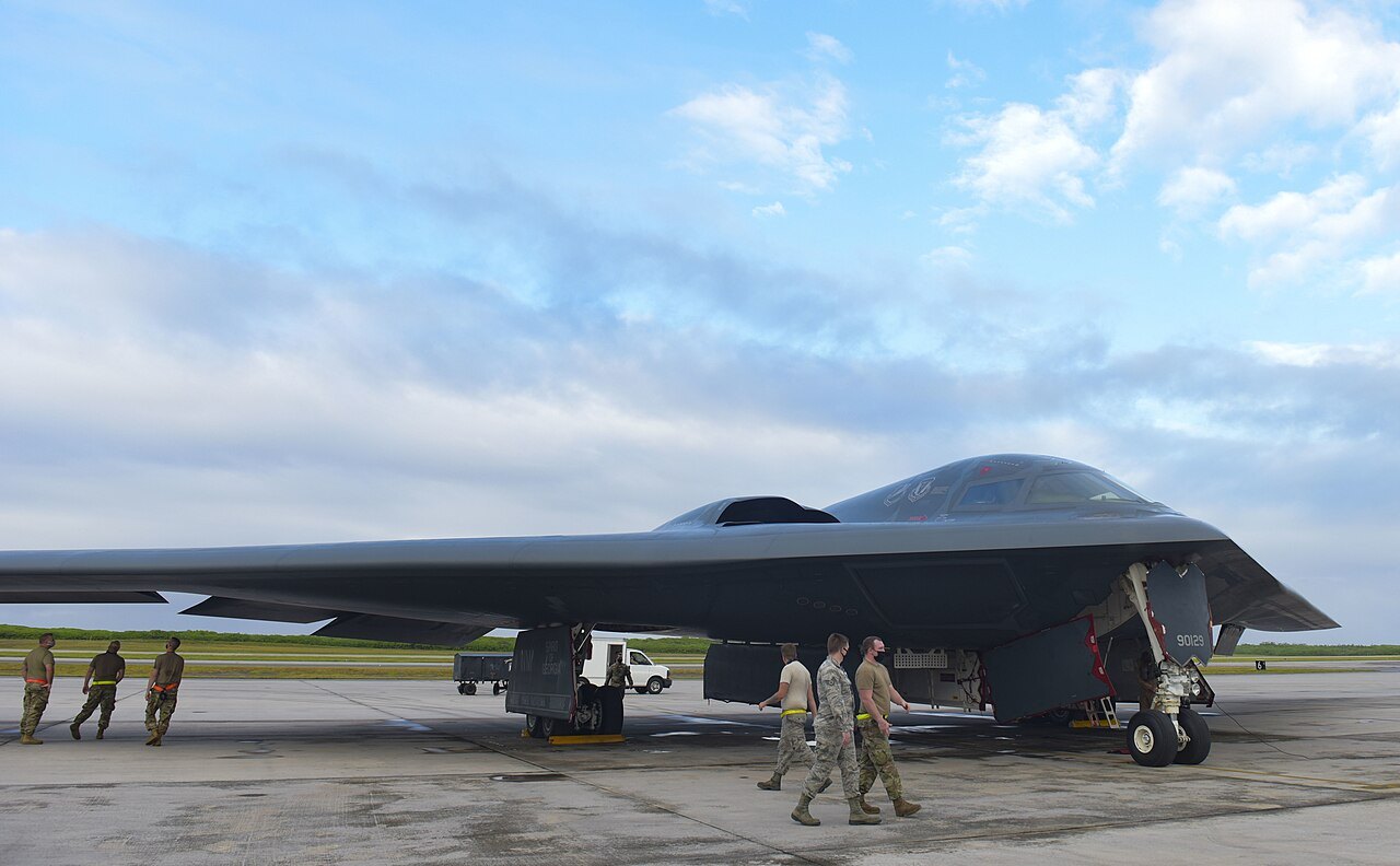 A US Air Force B-2 Spirit stealth bomber on the apron at Diego Garcia with ground crew walking beside it