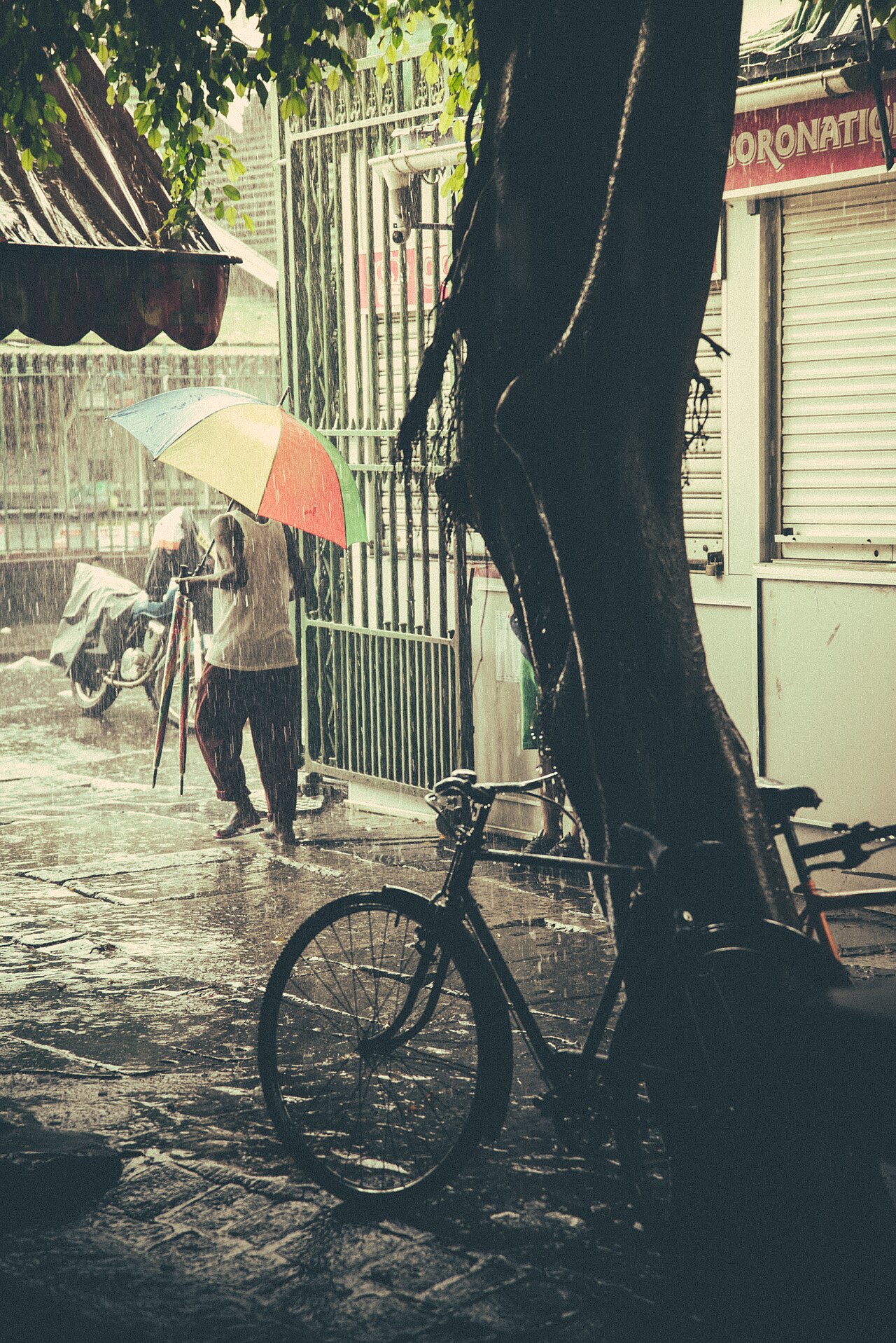 A man with a colourful umbrella walks past a bicycle and shuttered stalls in heavy rain near the Central Market in Port Louis