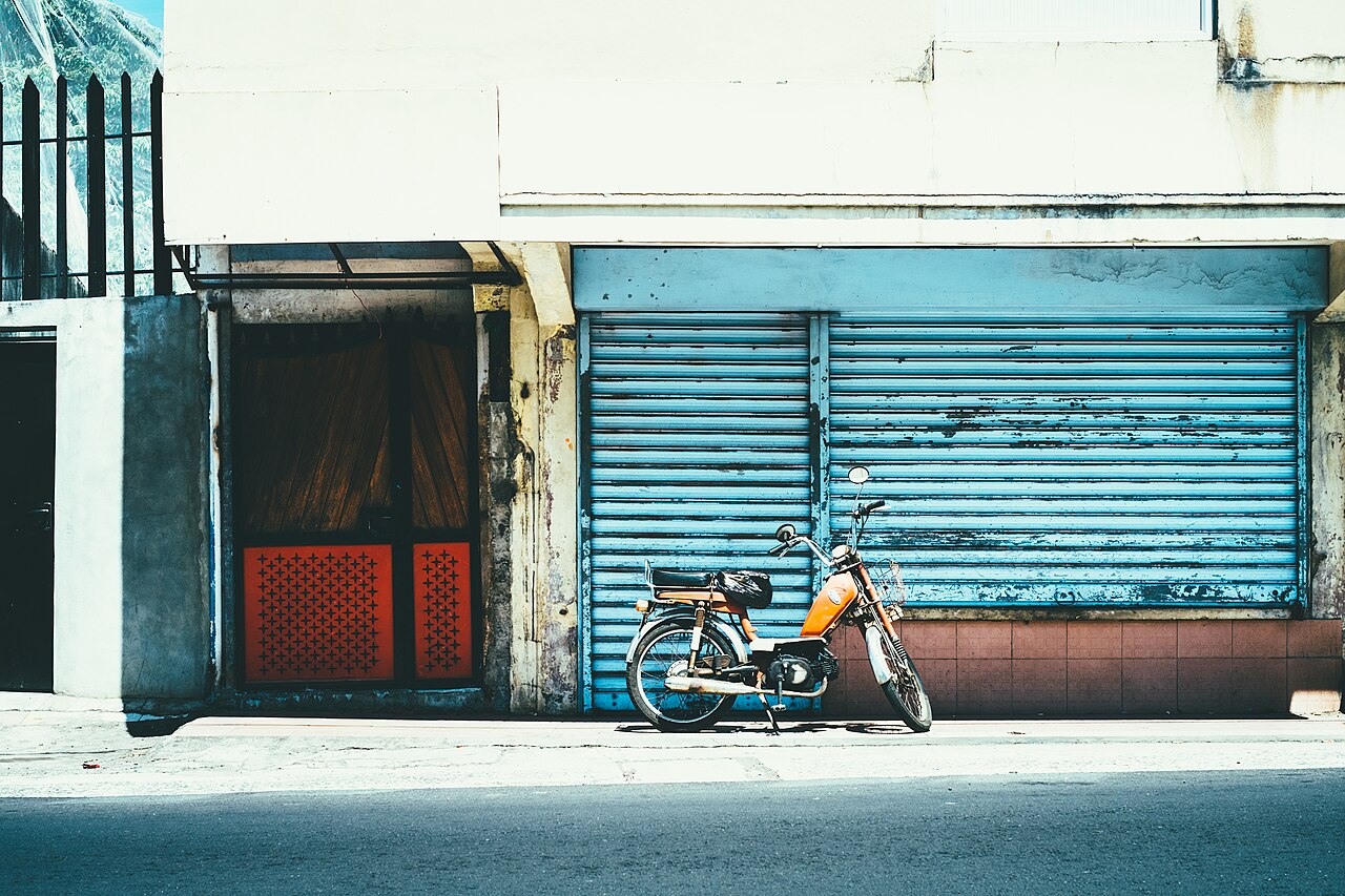 A parked orange moped in front of blue shutters on a street in Mauritius.