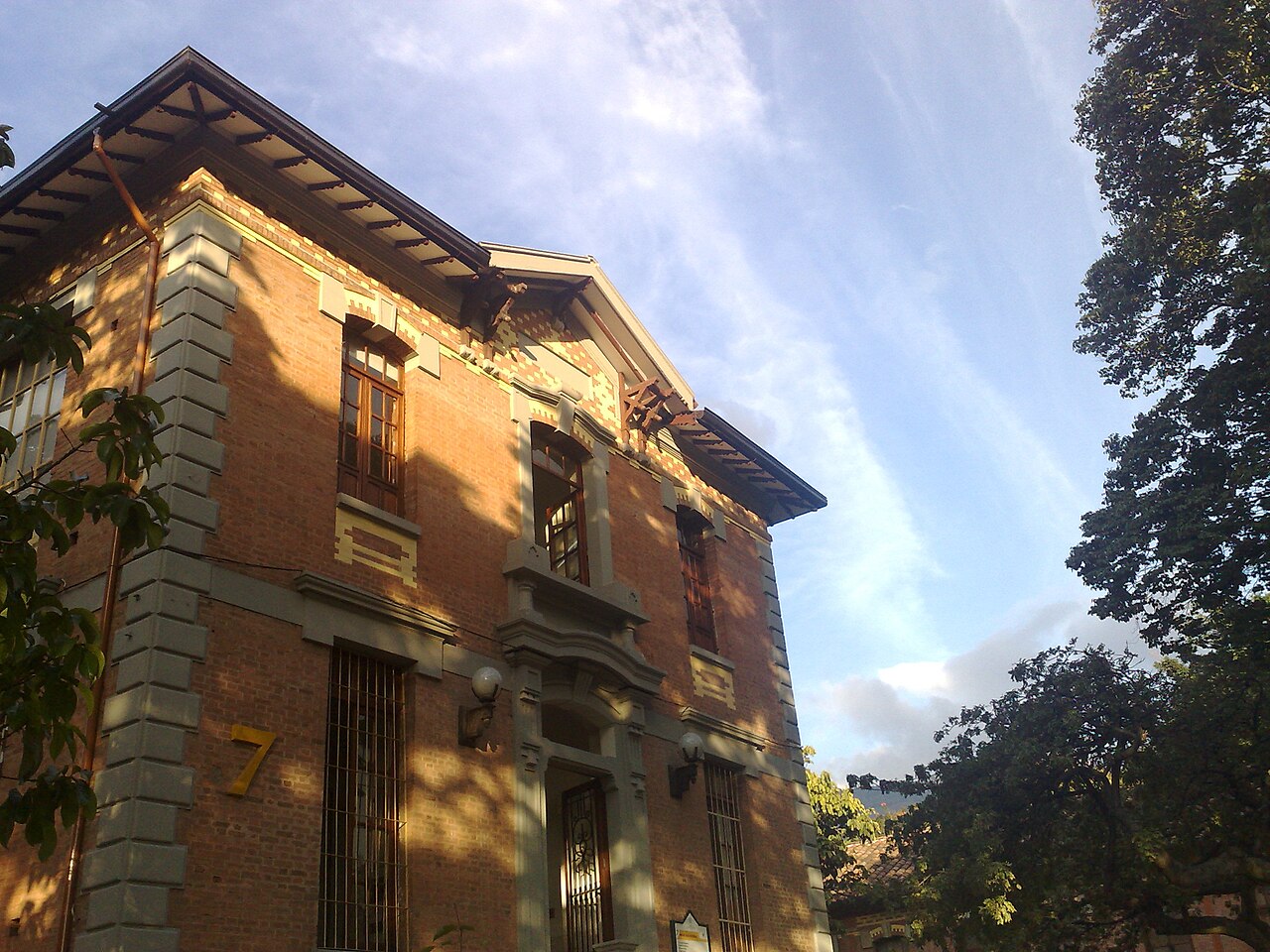 Red-brick hospital building with tall barred windows, a large number 7 on the wall and trees in late-afternoon light