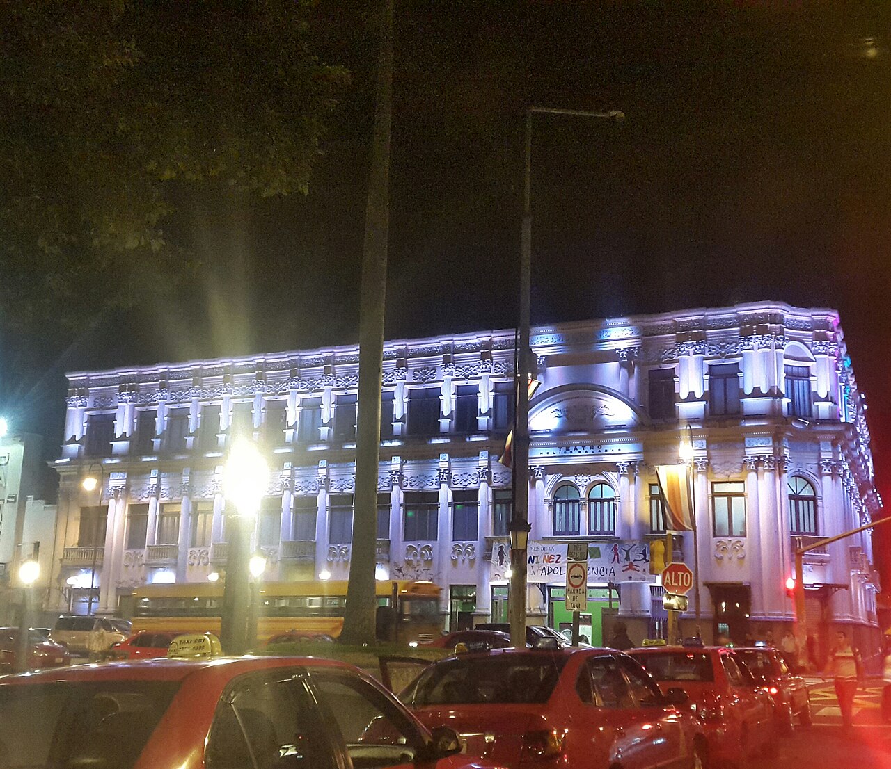 The Teatro Popular Melico Salazar lit up at night in San José, with red taxis in the foreground.