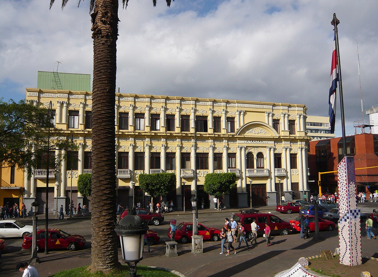 The Teatro Popular Melico Salazar in central San José, Costa Rica, with red taxis and a palm tree in the foreground.