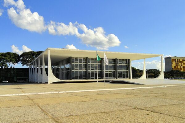 The white marble Supreme Federal Court building in Brasília under a blue sky, with two flagpoles in front of its glass facade