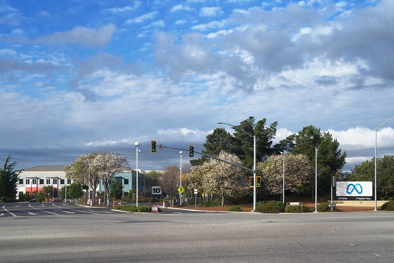 Entrance sign of Meta Platforms headquarters at 1 Hacker Way in Menlo Park, California, beside a road junction with traffic lights