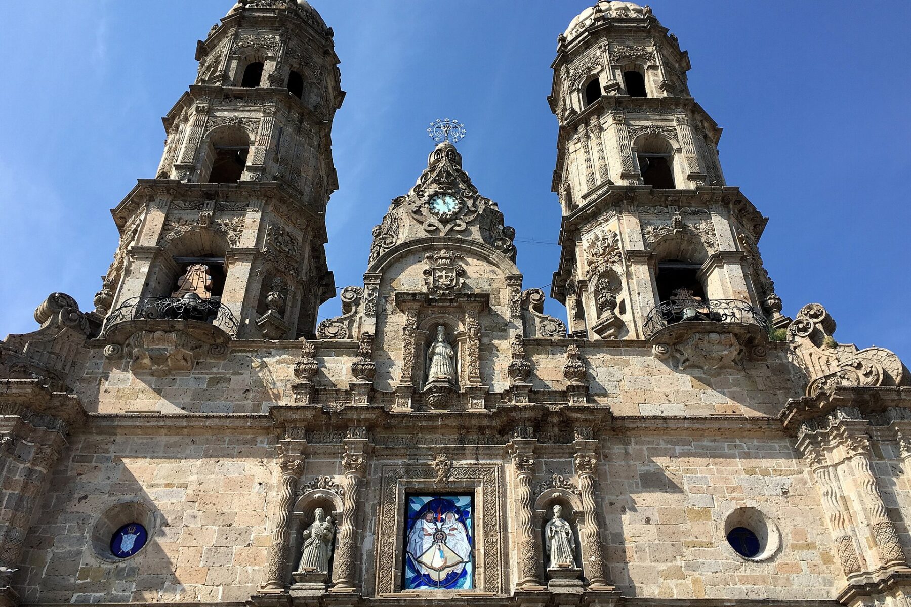 Twin bell towers and stone facade of the Basilica of Our Lady of Zapopan in Zapopan, Jalisco, Mexico, under a clear blue sky