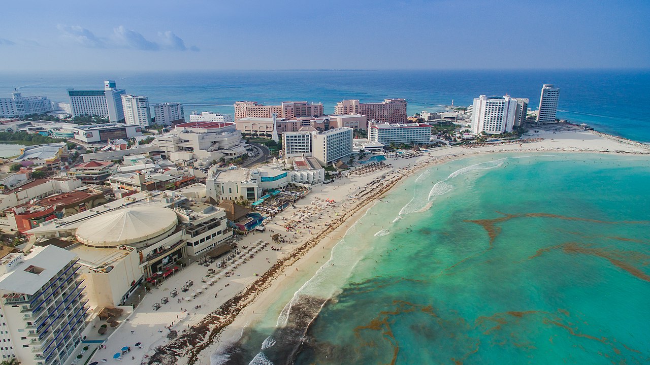 Aerial view of hotel towers and a white-sand beach on turquoise water in the hotel zone of Cancún