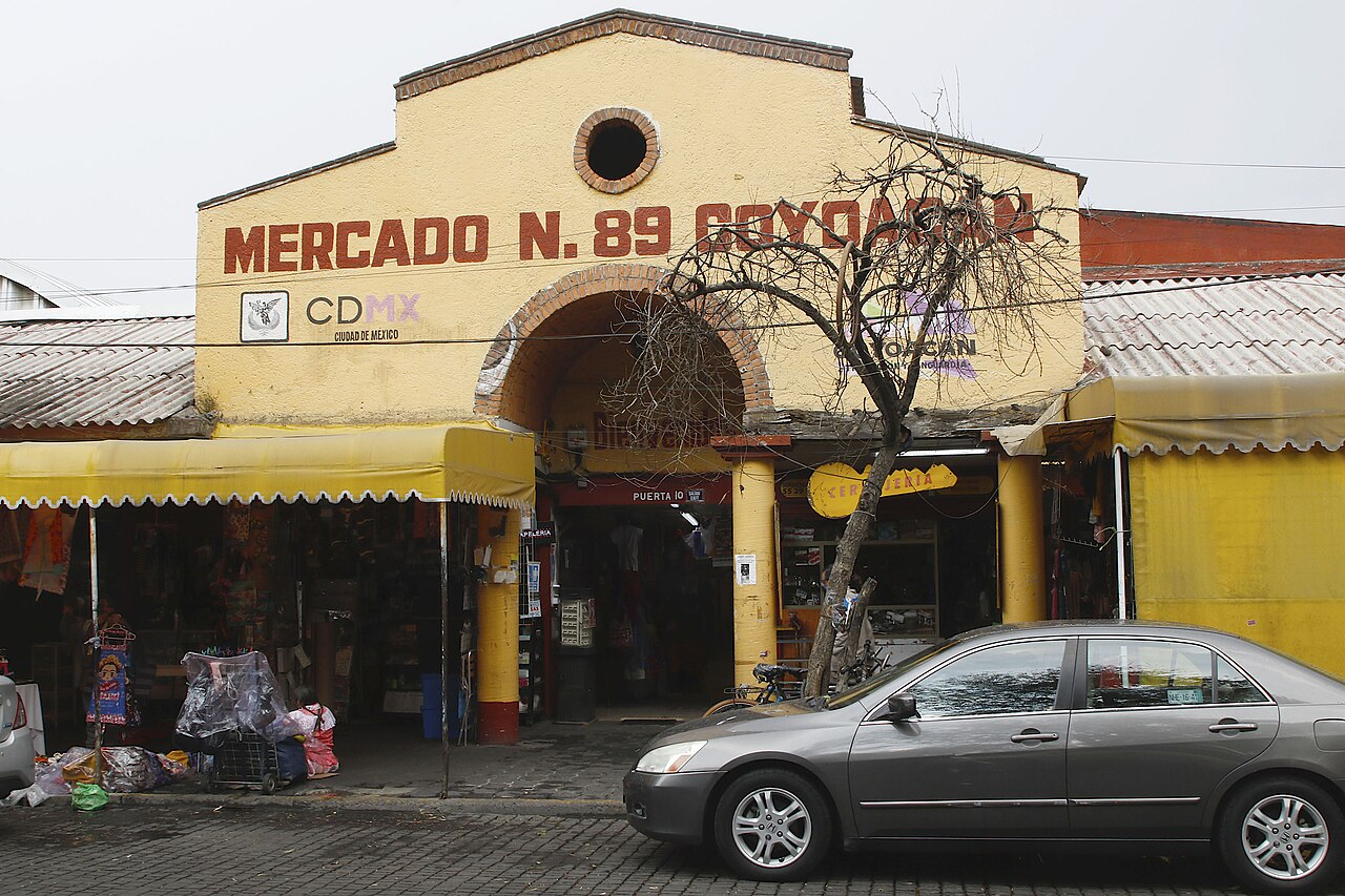 The yellow entrance of Mercado 89 in Coyoacán, Mexico City, with market stalls under awnings and a car parked in front.