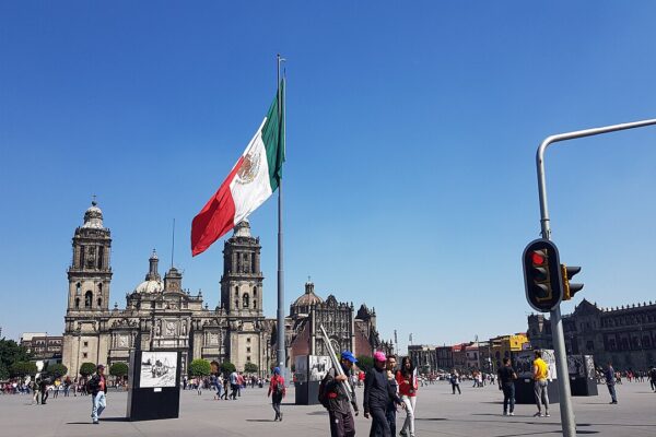 The Zócalo main square in Mexico City with the Metropolitan Cathedral and a large Mexican flag under a blue sky.