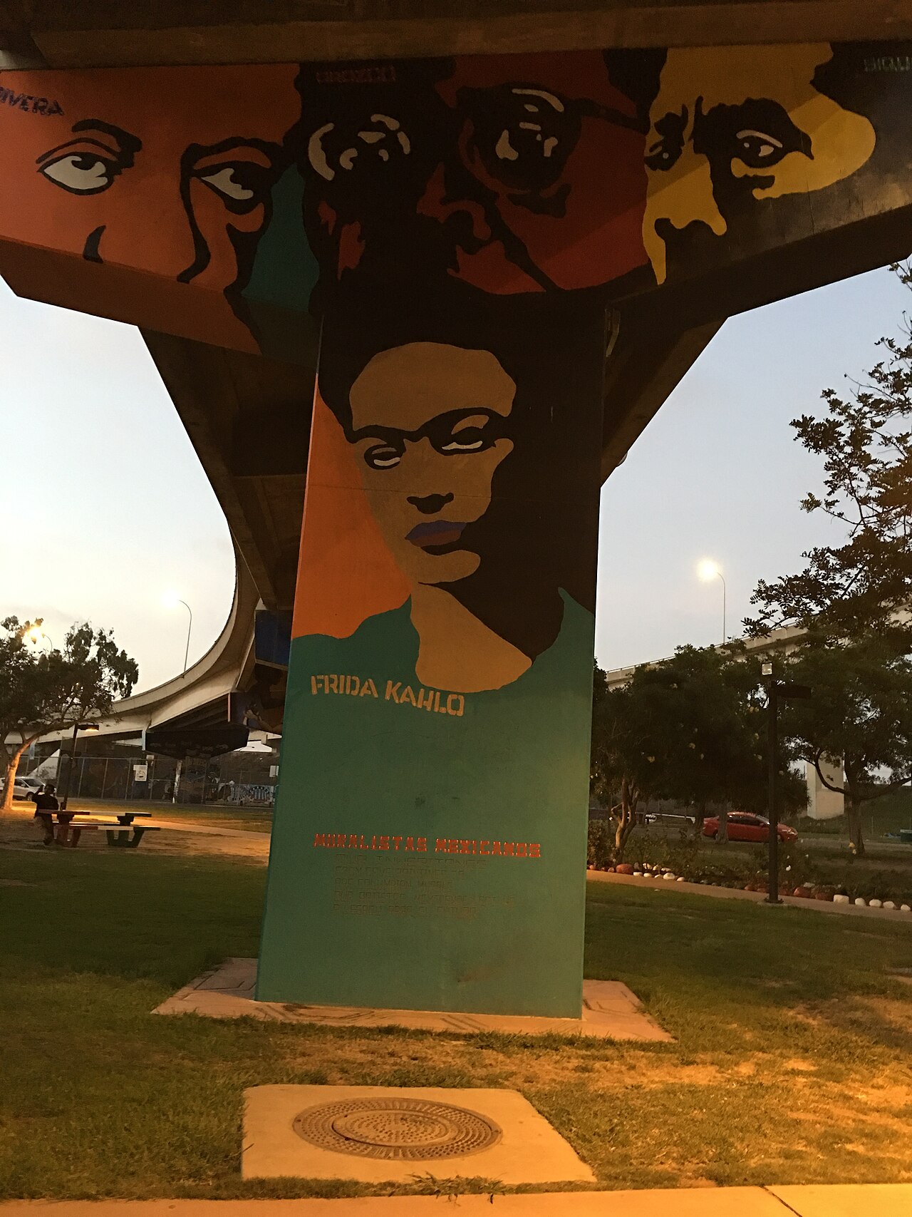 A painted portrait of the Mexican artist Frida Kahlo on a concrete pillar at Chicano Park in San Diego at dusk.