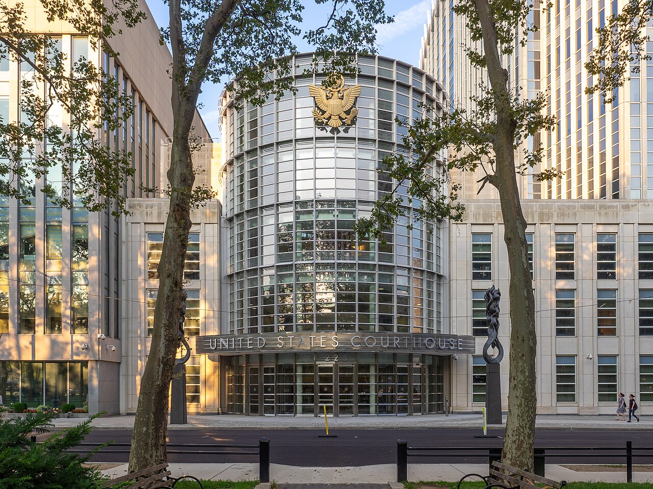 Curved glass entrance of the United States Courthouse in Brooklyn with a gilded eagle above the doors and plane trees in front