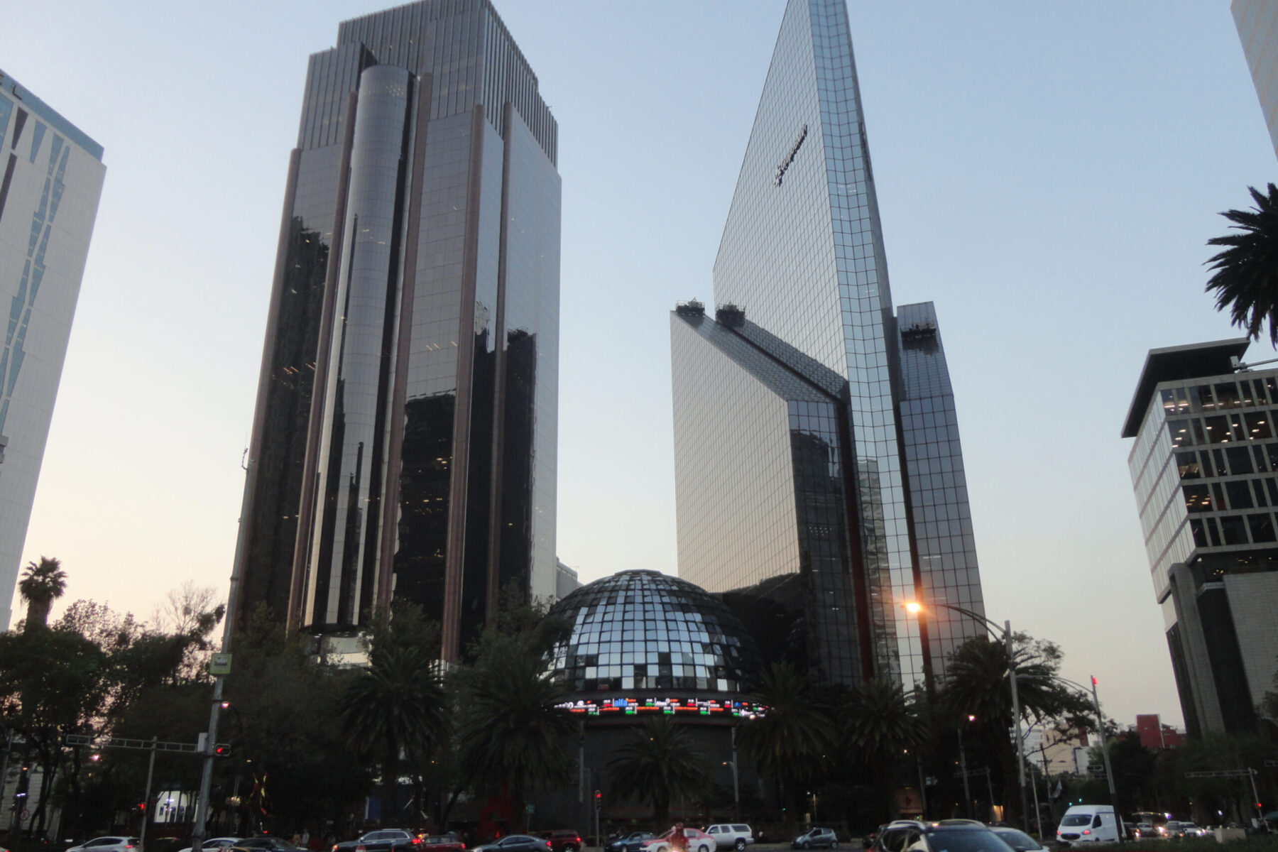The glass dome of the Mexican Stock Exchange at dusk, between two tall office towers on Paseo de la Reforma in Mexico City