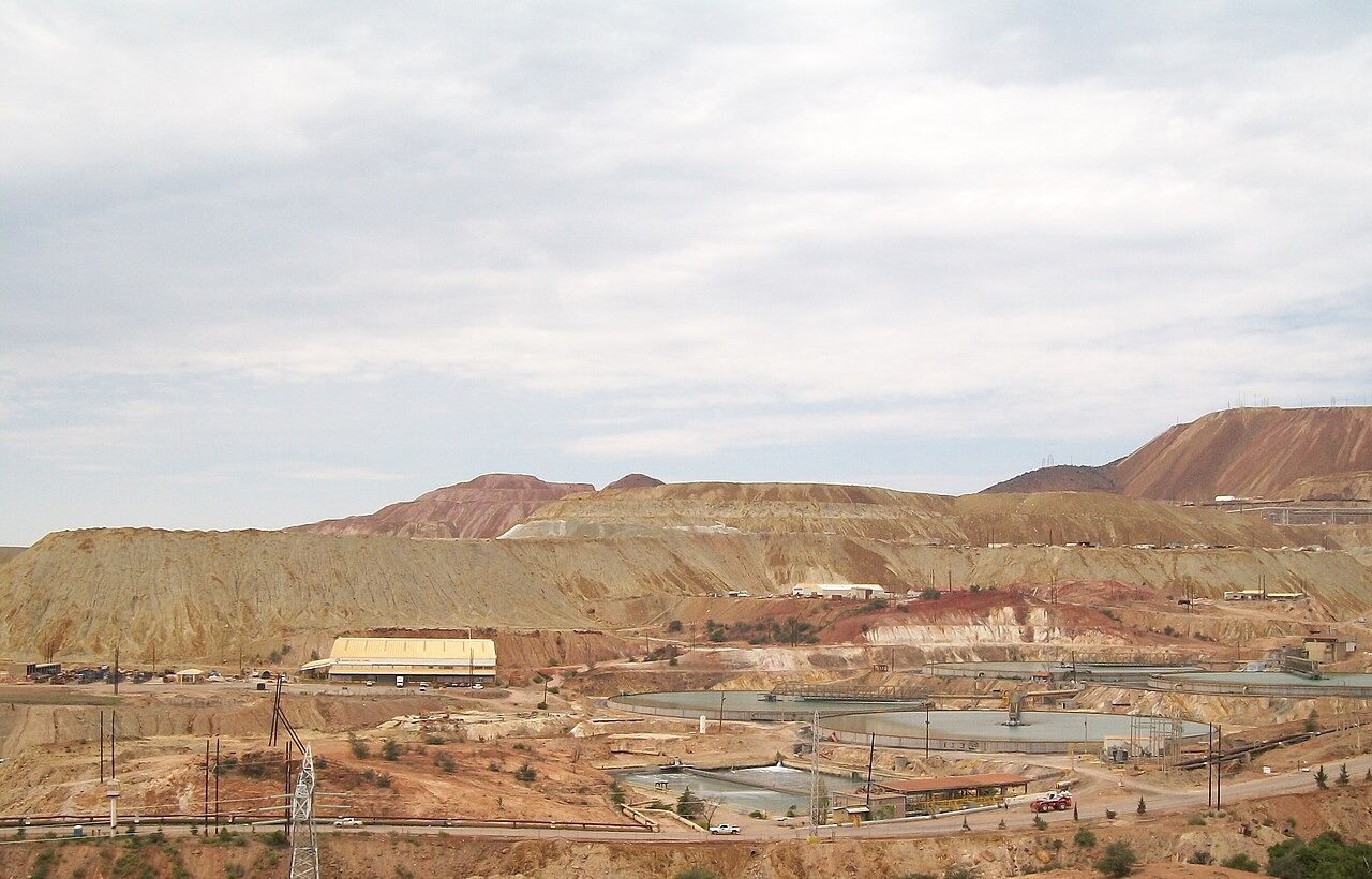 Terraced waste heaps and round water ponds of an open-pit copper mine in the dry hills of Cananea, Sonora, under a grey sky