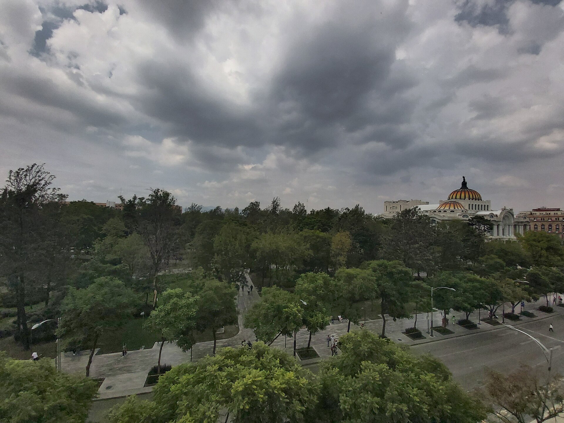 Alameda Central park and the dome of the Palacio de Bellas Artes under a cloudy sky in Mexico City