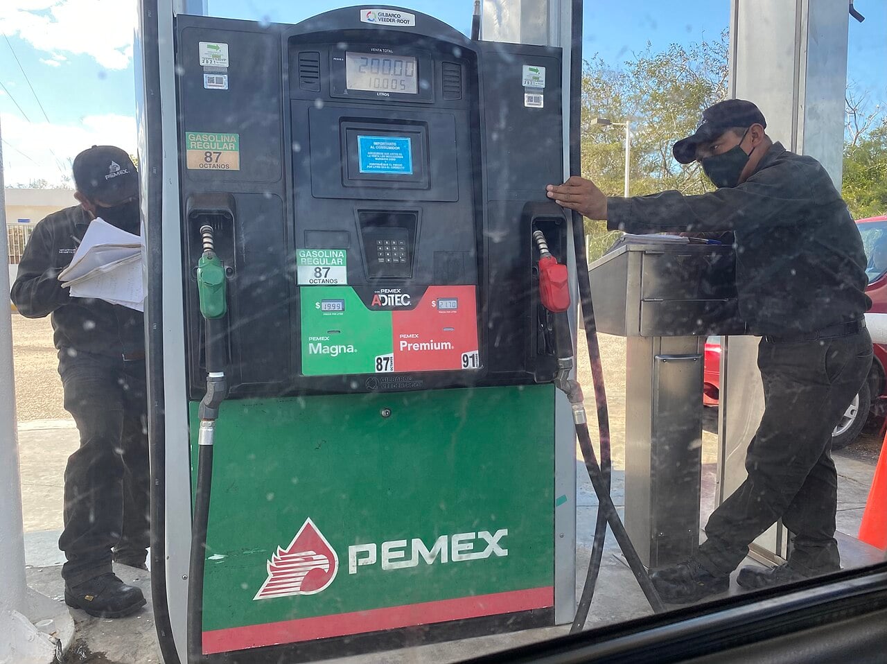 A Pemex fuel pump with Magna regular and Premium gasoline nozzles, with two station attendants beside it