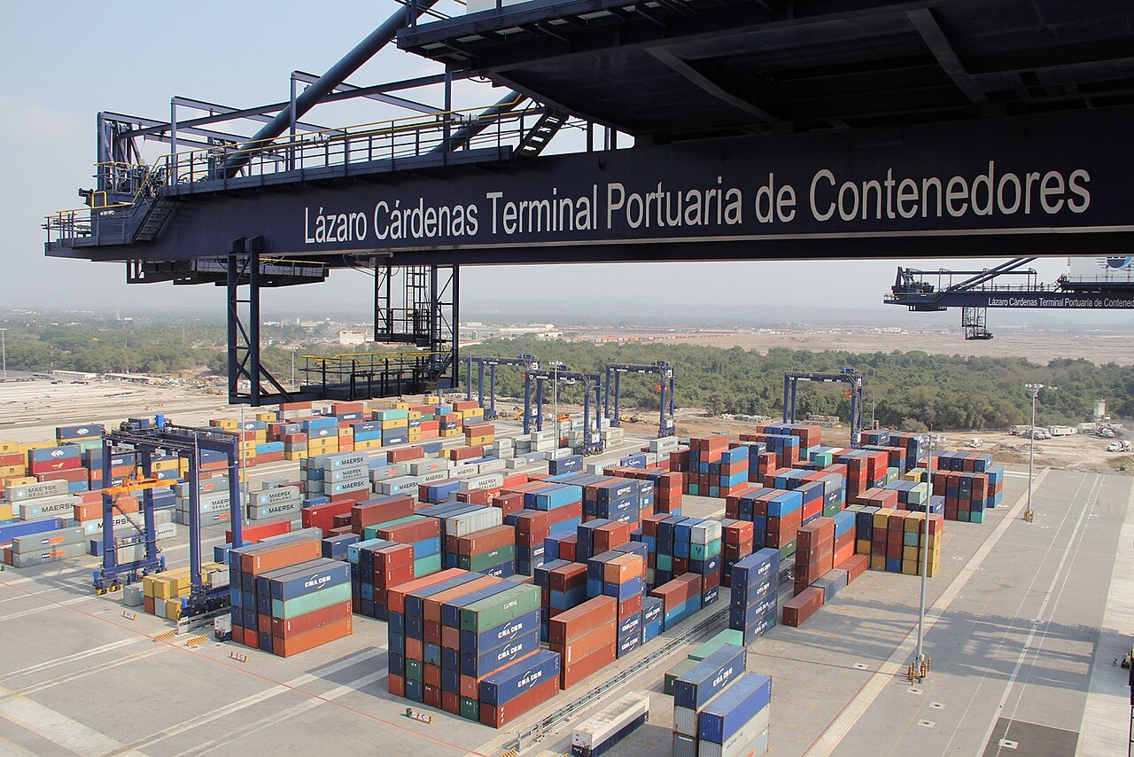Stacks of shipping containers under a gantry crane marked Lázaro Cárdenas Terminal Portuaria de Contenedores at the port of Lázaro Cárdenas, Mexico