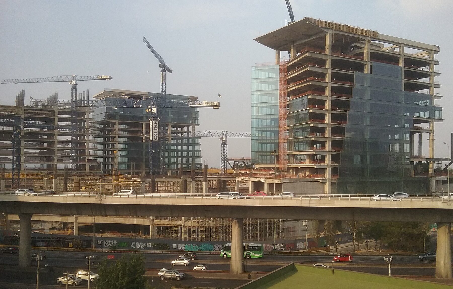 Office towers under construction with tower cranes beside an elevated highway in Mexico City