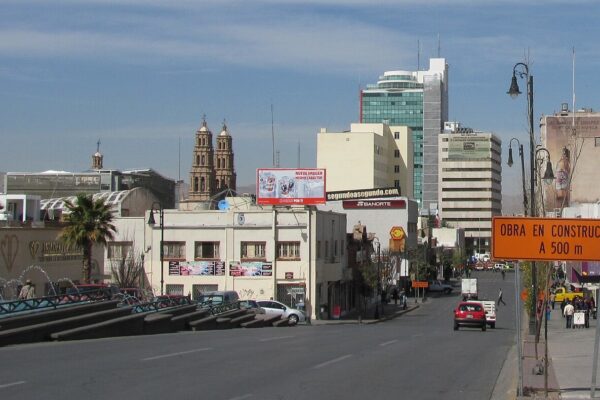 Downtown street in Chihuahua City, Mexico, with the twin bell towers of the cathedral behind low buildings and a blue sky
