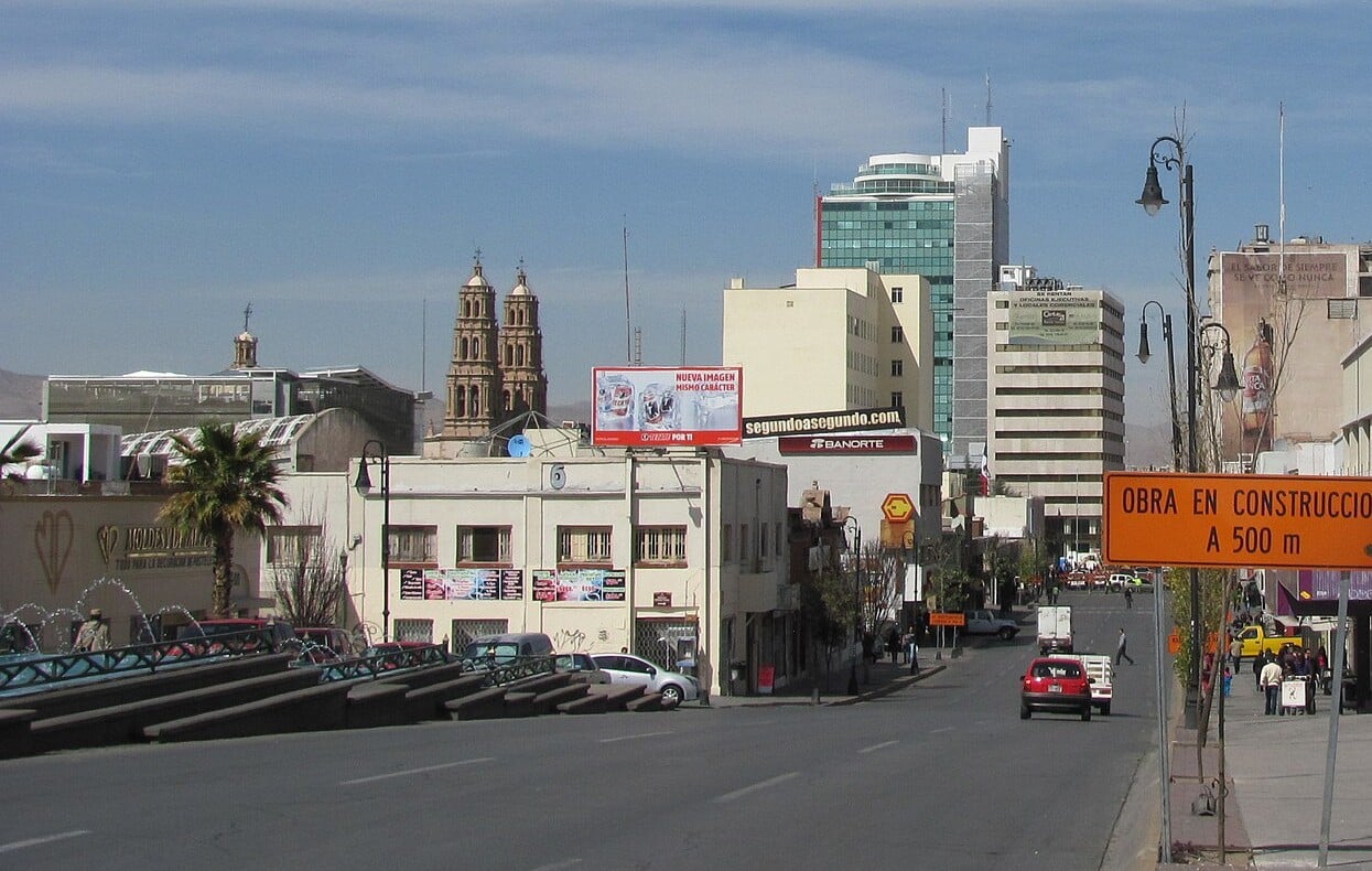 Downtown street in Chihuahua City, Mexico, with the twin bell towers of the cathedral behind low buildings and a blue sky