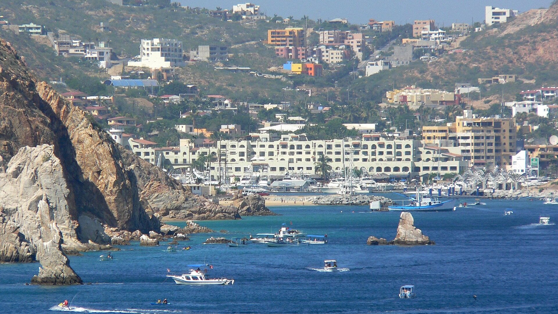 Boats and hotels around the harbor and marina of Cabo San Lucas on a clear day, seen from the water