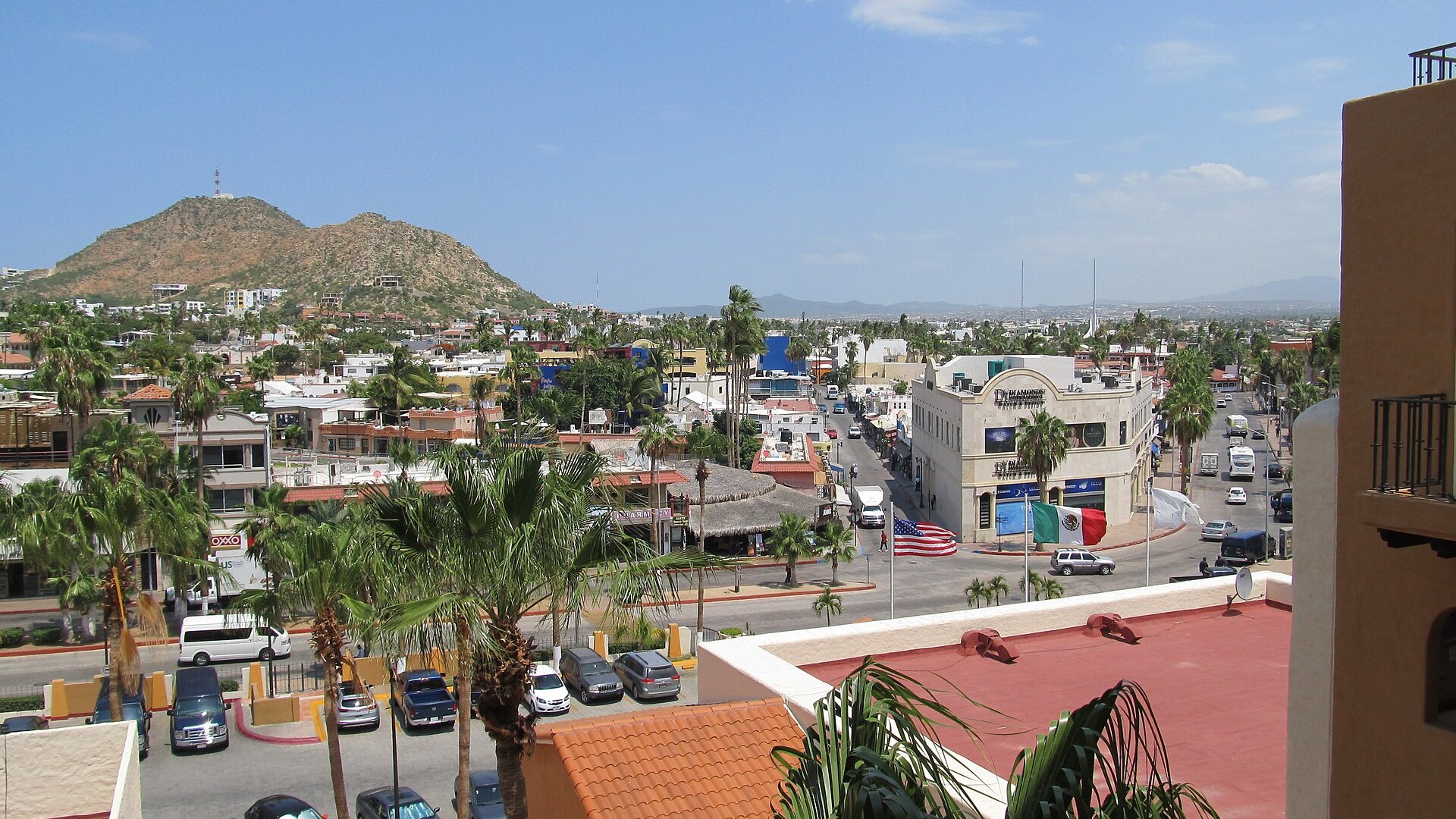 A street in the town center of Cabo San Lucas with palm trees, shops and a hill in the background on a sunny day