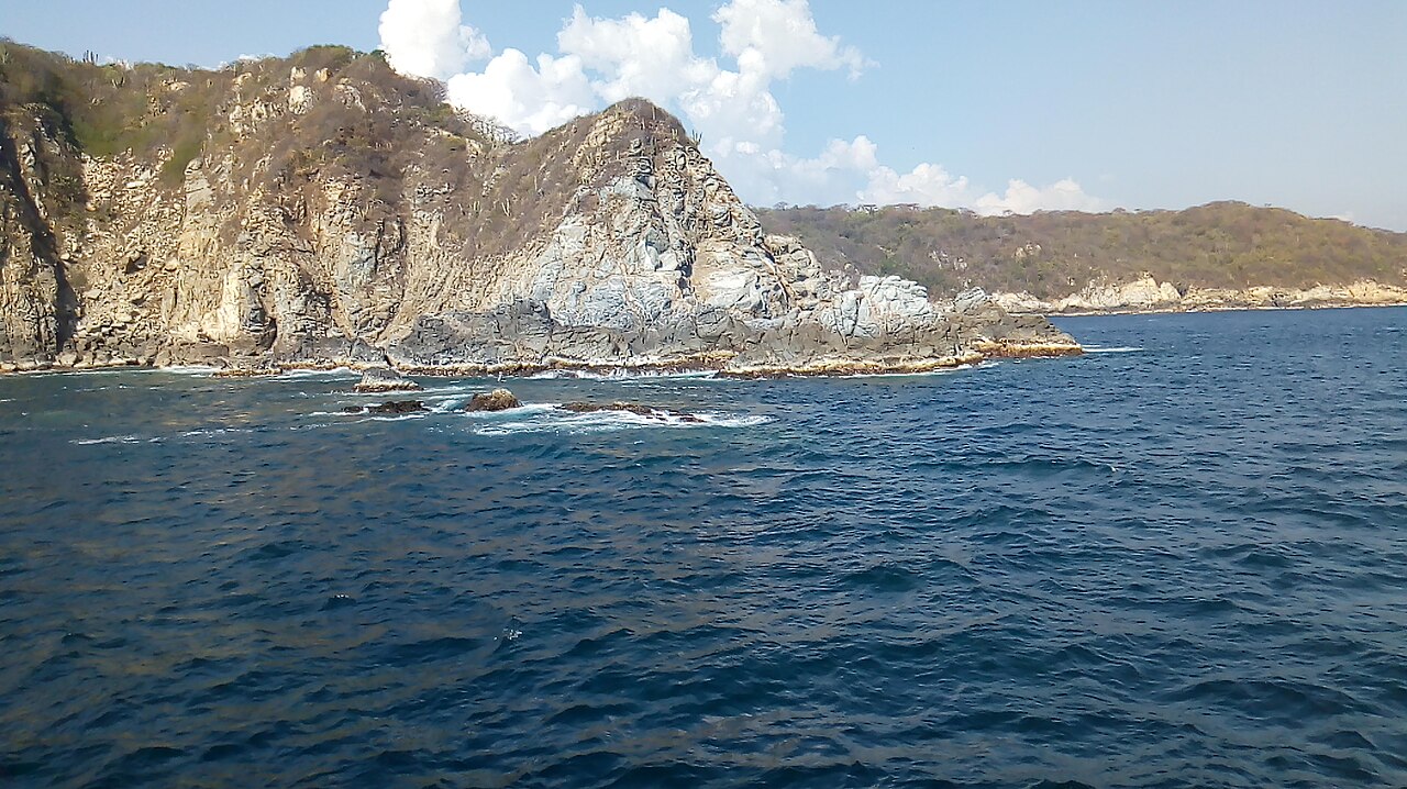 Rocky cliffs covered with dry scrub rise from the deep blue Pacific Ocean along the Huatulco coast