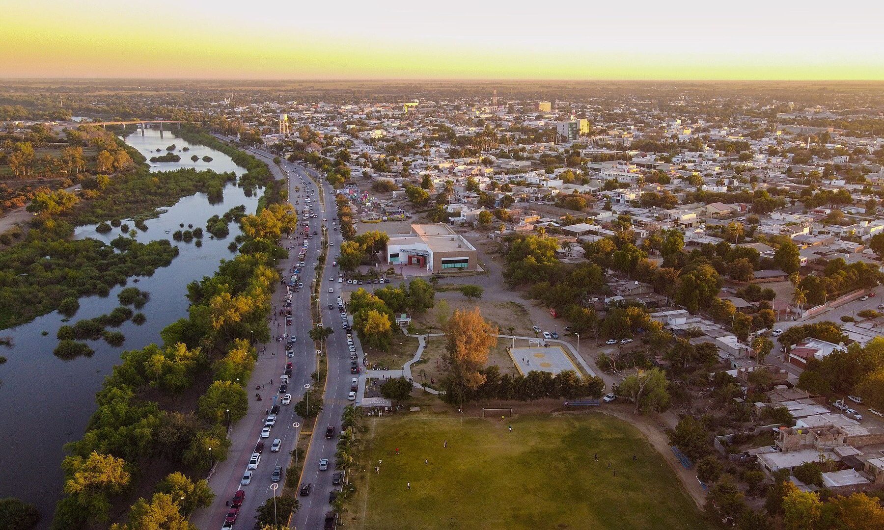 Aerial view of the city of Guasave in northern Sinaloa, Mexico, with a tree-lined river, a main road and houses at sunset