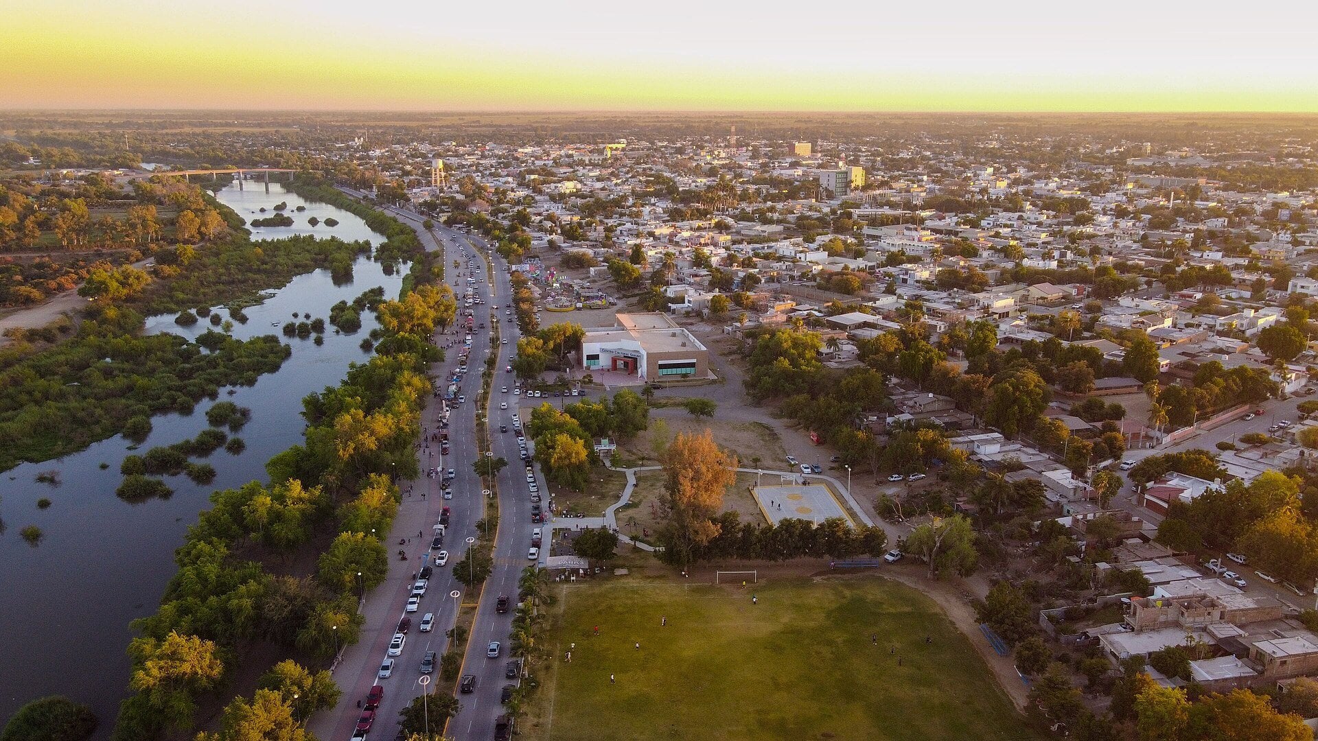 Aerial view of the city of Guasave in northern Sinaloa, Mexico, with a tree-lined river, a main road and houses at sunset