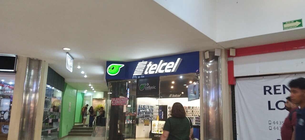 A Telcel mobile phone shop with a blue illuminated sign inside a shopping centre, with a customer walking towards the counter