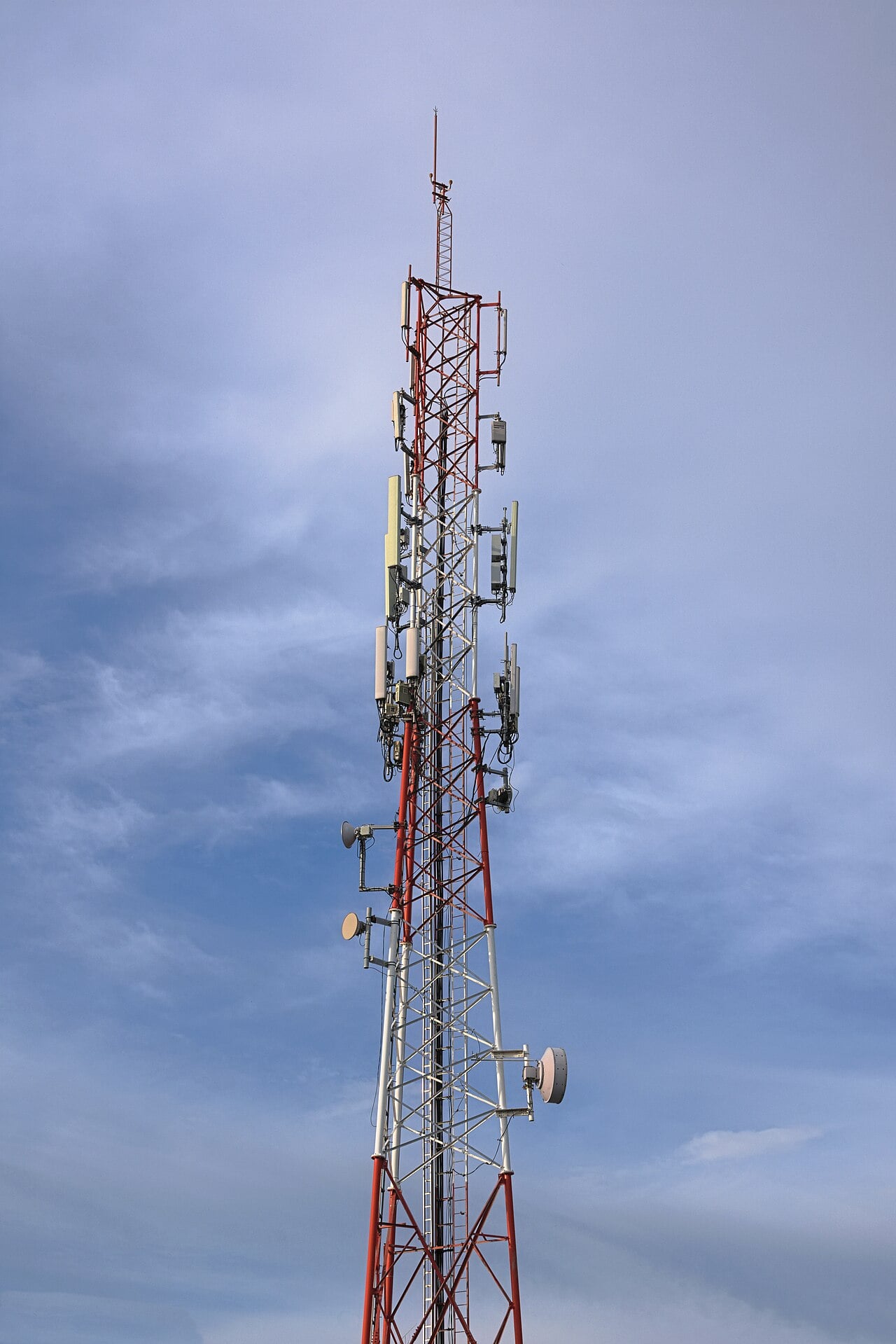 A red and white lattice mobile phone tower fitted with antennas and microwave dishes against a blue sky