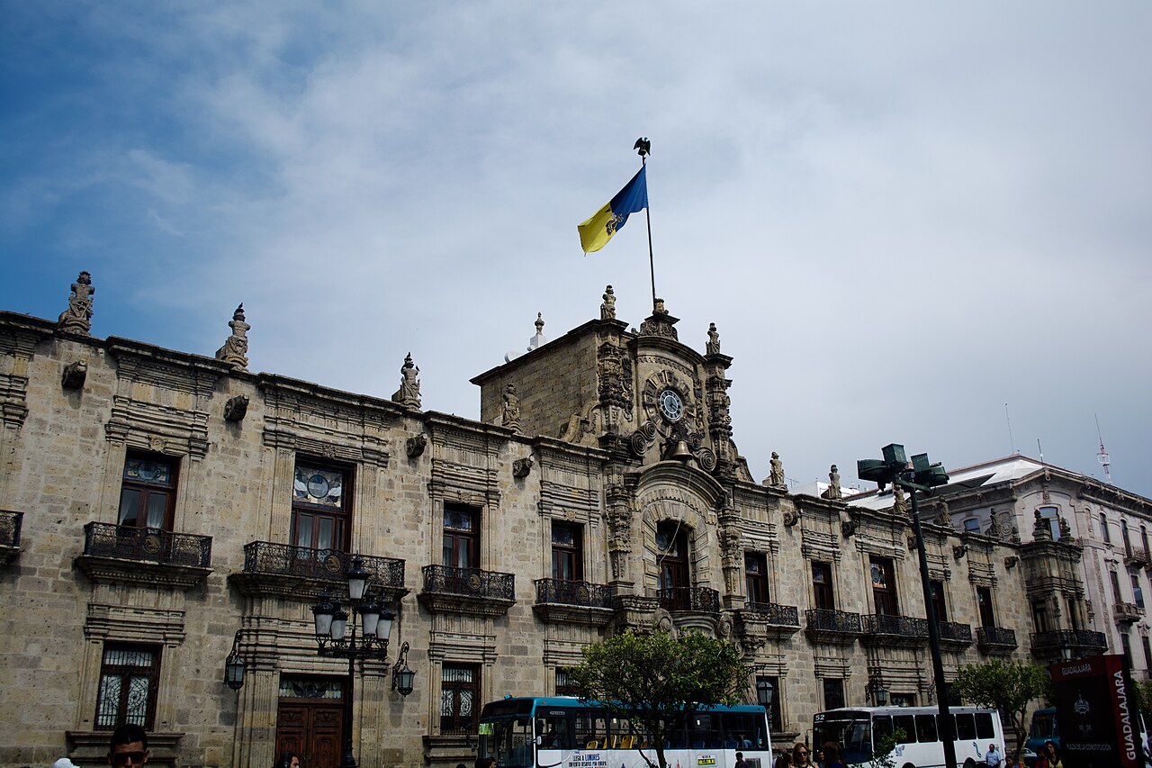 Stone facade of the Jalisco Government Palace in Guadalajara with the state flag flying above the clock tower